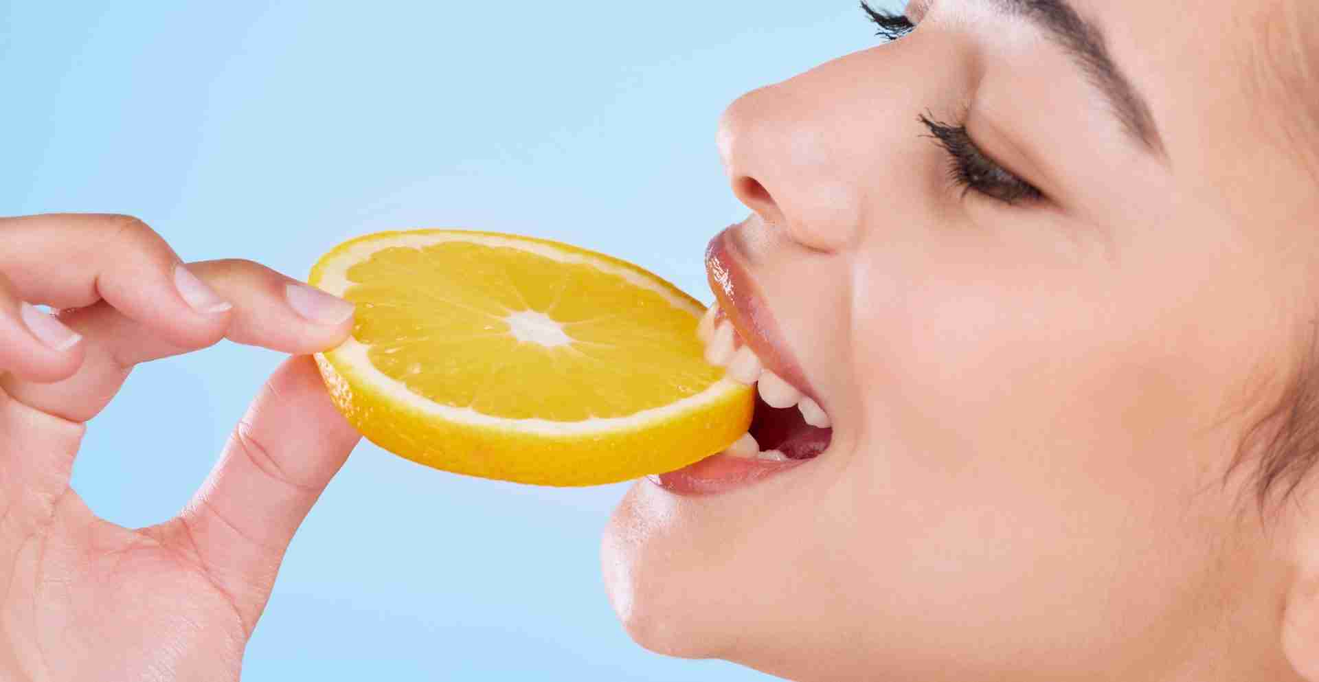 Studio shot of an attractive young woman biting into a slice of orange against a blue background Ragazza mangia arancia per integrare vitamine e minerali per denti
