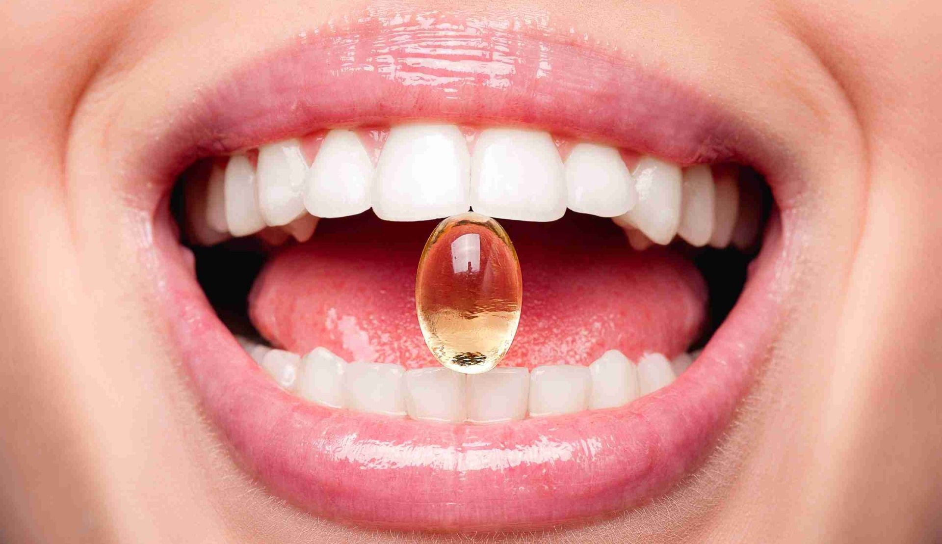 Close Up Of Beautiful Woman Opened Mouth Holding Fish Oil Pill In White Teeth. Smiling Girl Holding Capsule With Omega-3 Between Teeth. Healthy Diet Nutrition Concept integrazione vitamine e minerali per denti